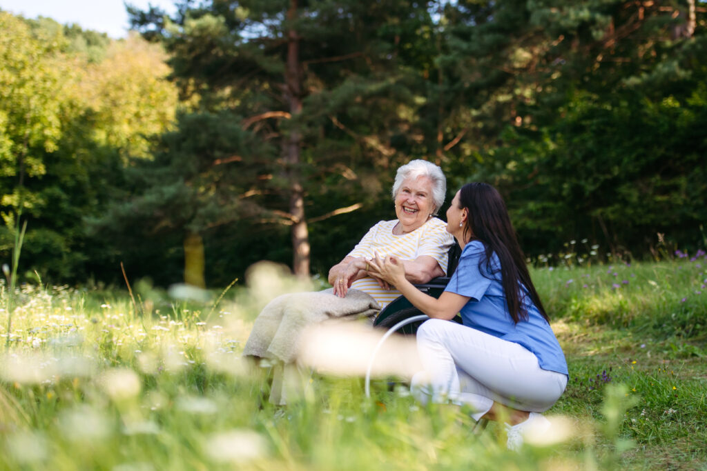 Pflegekraft und Seniorin im Rollstuhl unterwegs an einem Frühlingstag