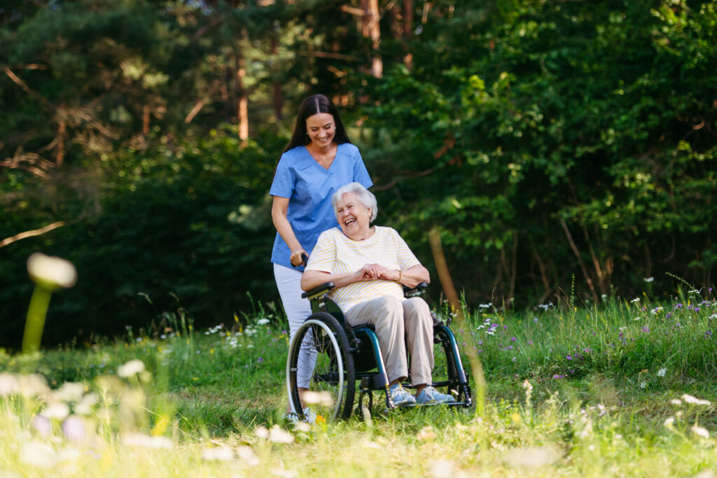 Pflegekraft und Seniorin im Rollstuhl bei einem Spaziergang im Frühling